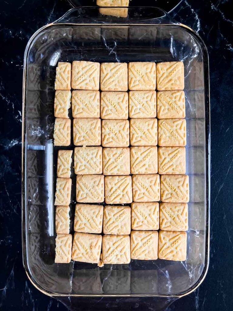 Shortbread cookies in a single layer in the bottom of a glass baking dish on a dark surface.