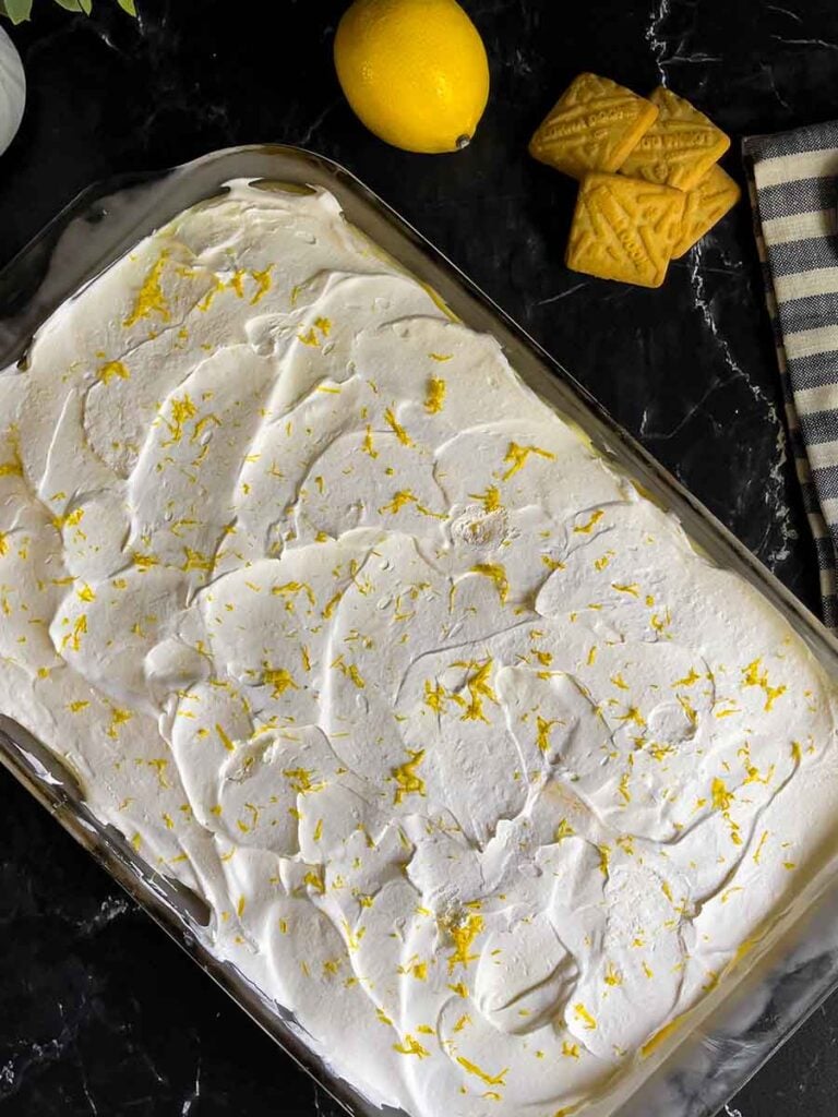 Lemon Icebox Cake on a dark surface with a lemon and shortbread cookies in the background.