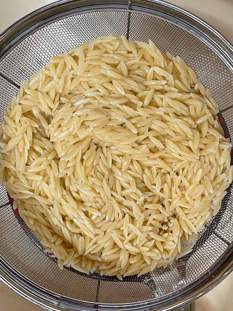 Cooked and drained orzo in a mesh strainer for the spinach and feta orzo salad.