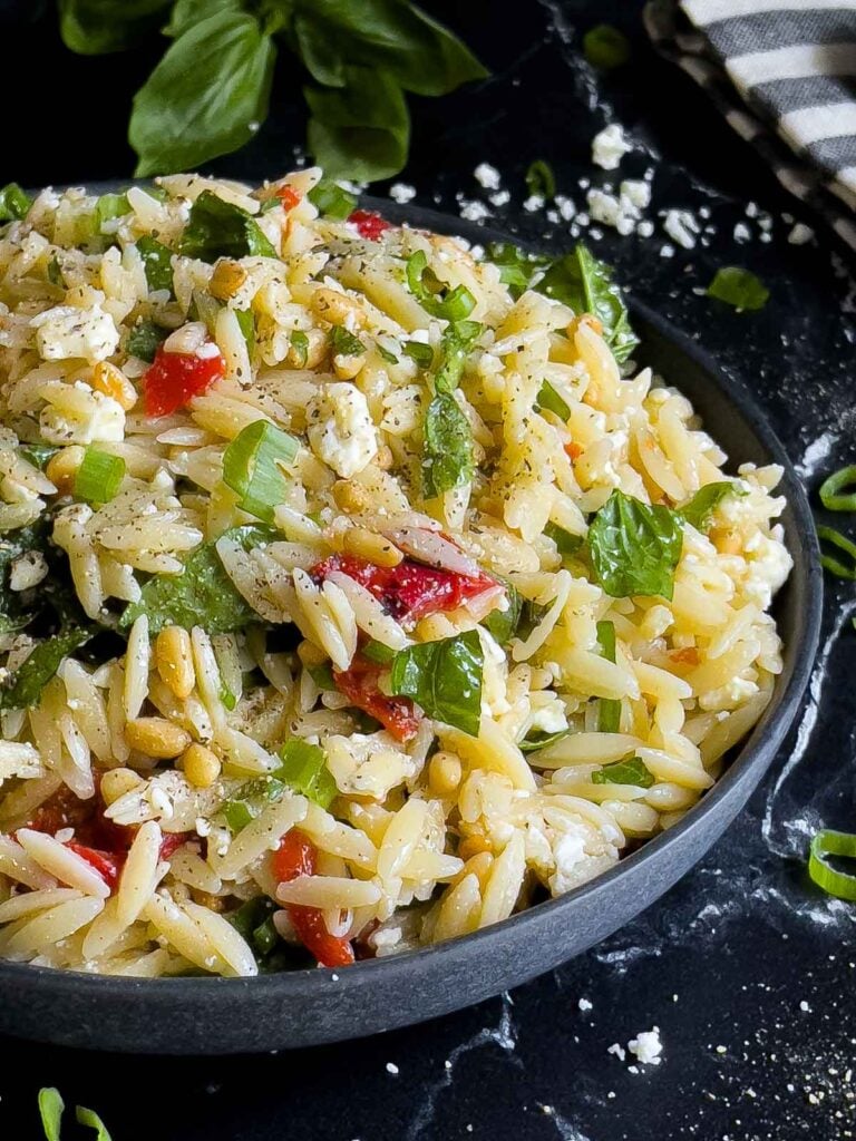 Spinach and Feta Orzo Salad in a dark bowl on a dark surface.