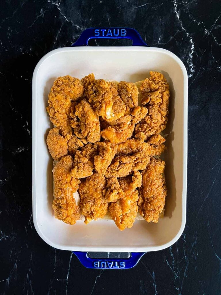 Chicken tenders layered on the bottoms of slider rolls in a 9x13 baking dish.