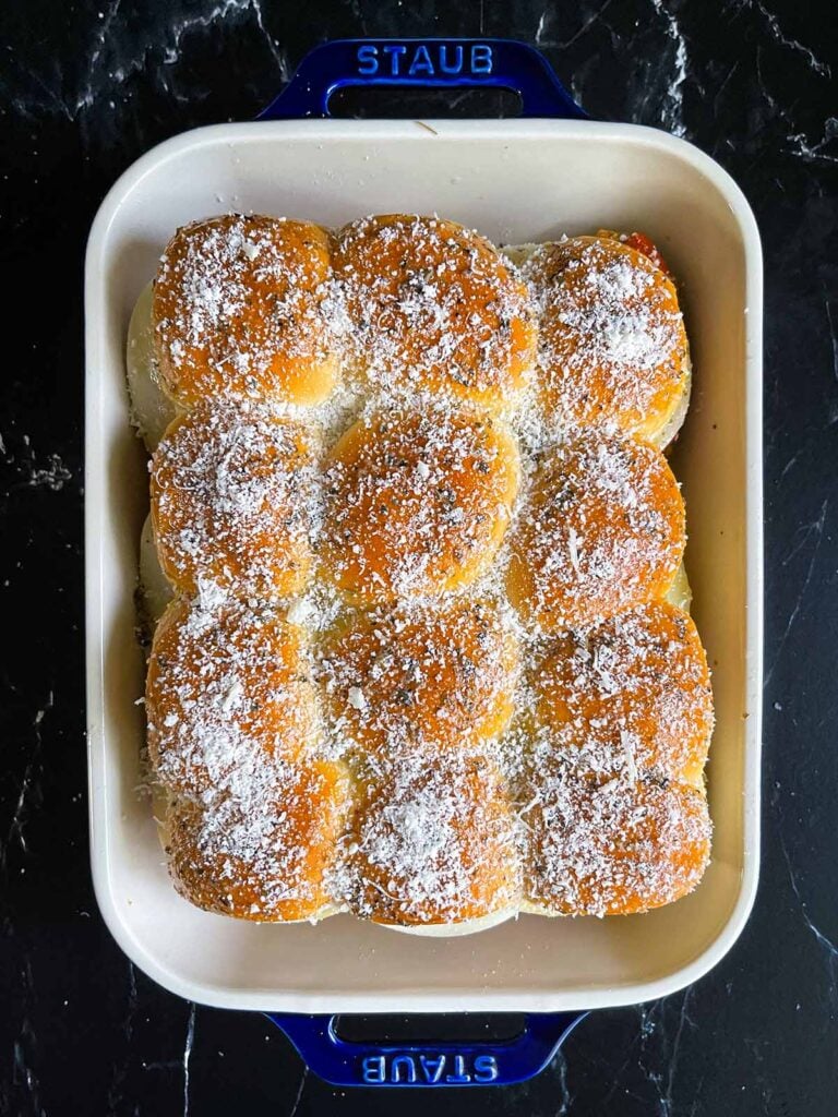 Chicken parmesan sliders topped with grated parmesan cheese in a 9x13 inch baking dish.