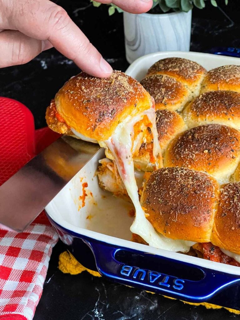 A chicken parmesan slider being removed from the baking dish.