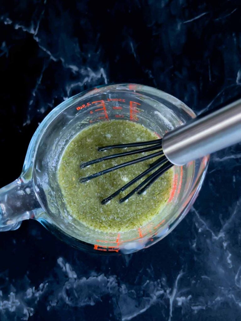 Seasoning mix for Dill Pickle Chex mix in a glass measuring cup on a dark surface.