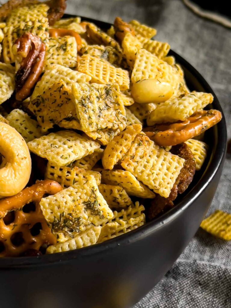 Dill Pickle Chex Mix in a small dark bowl on a light linen napkin.