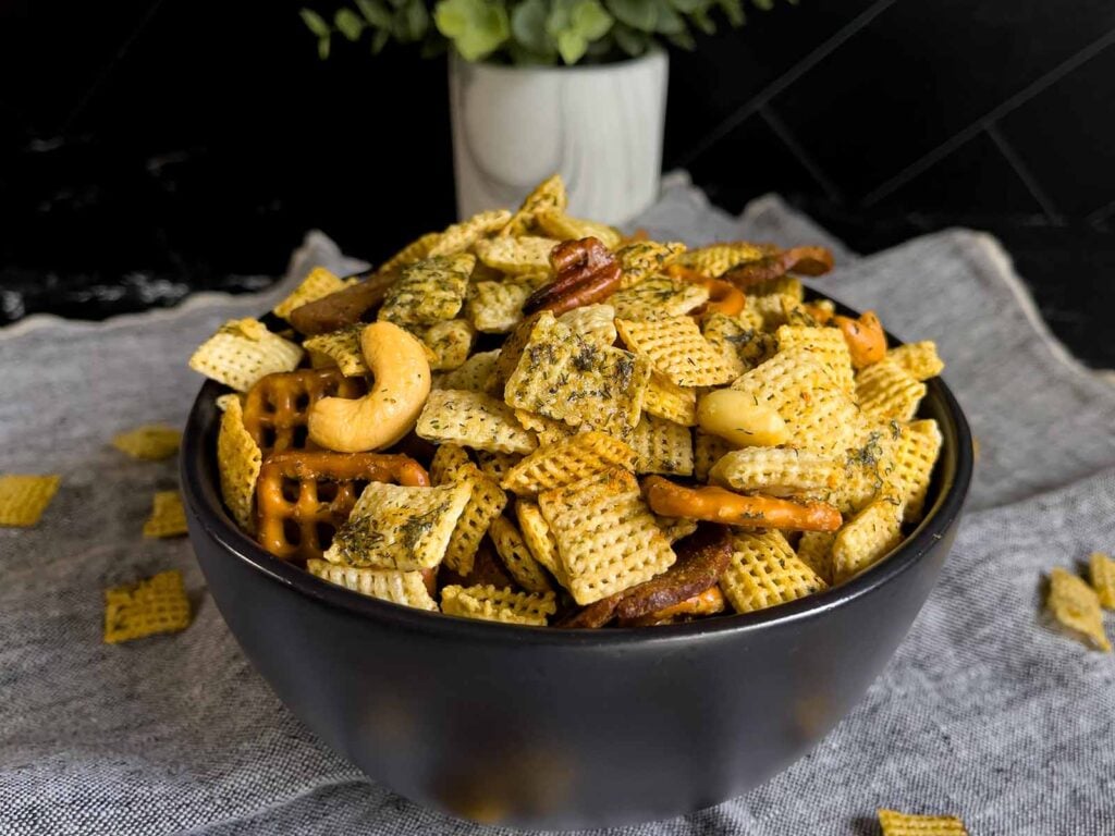 Dill Pickle Chex Mix in a small dark bowl on a light linen napkin.