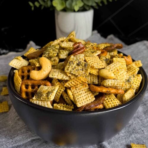 Dill Pickle Chex Mix in a small dark bowl on a light linen napkin.