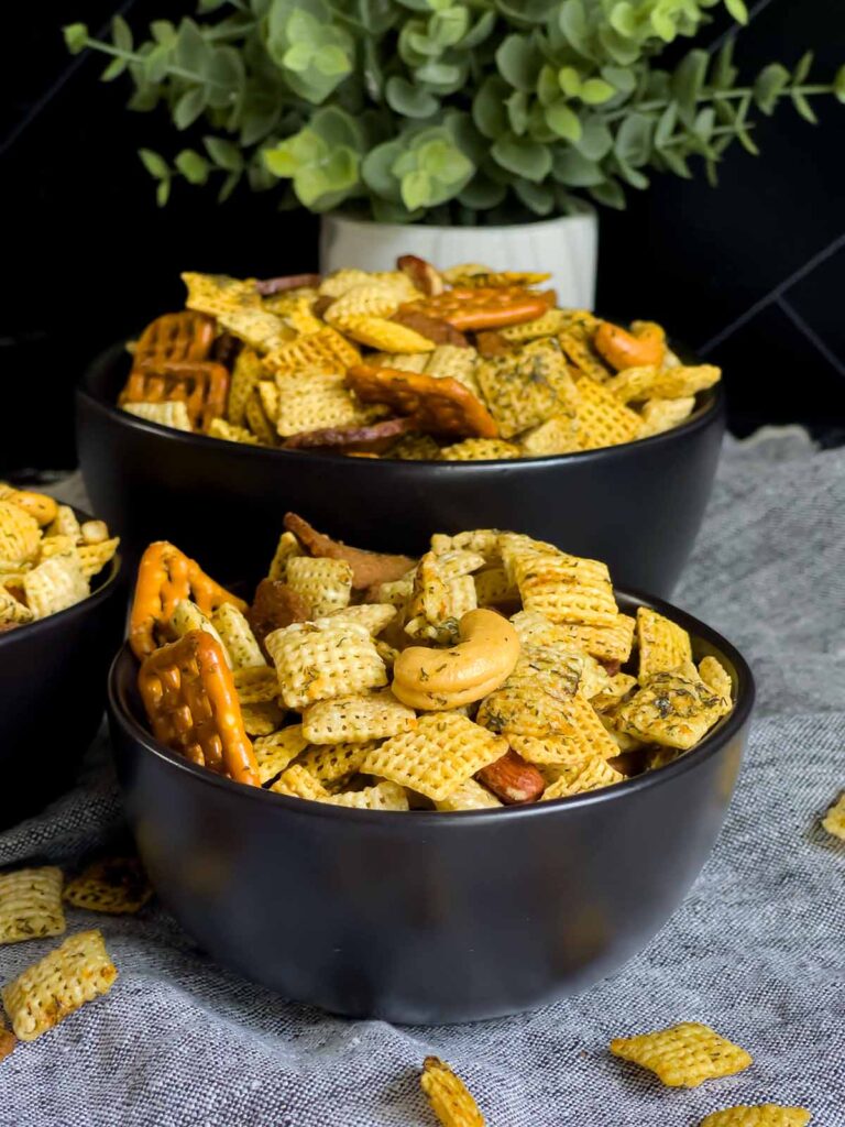 Dill Pickle Chex Mix in a three dark bowls on a light linen napkin.