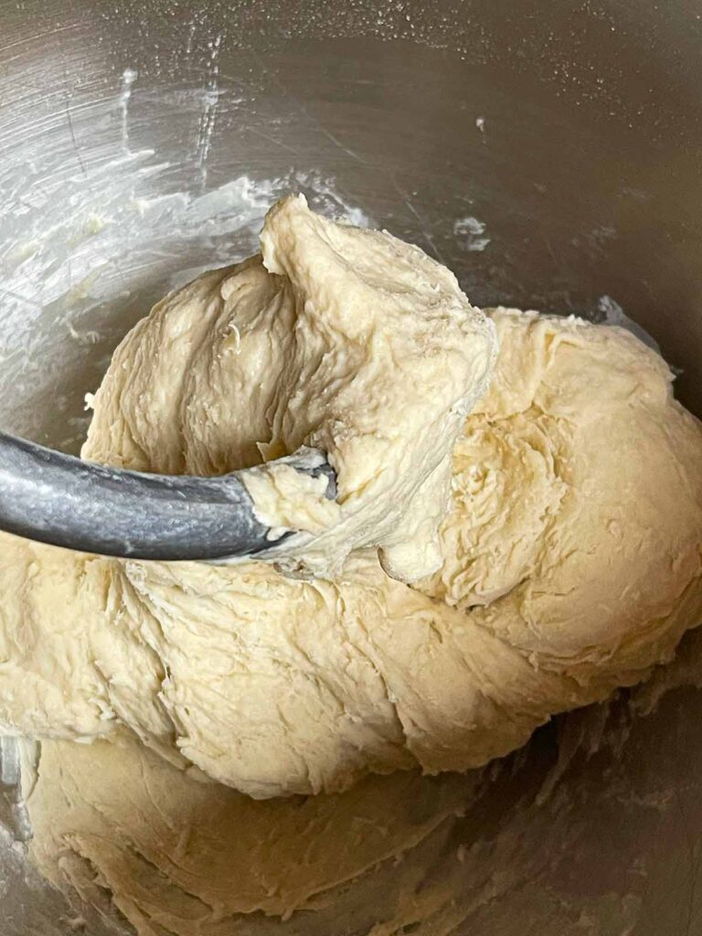 Pizza dough being mixed in a stand mixer bowl.