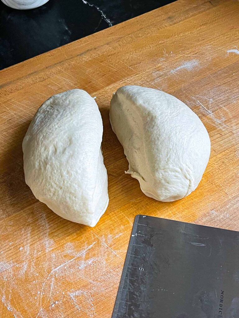 Pizza dough split into two portions on a large wooden cutting board.