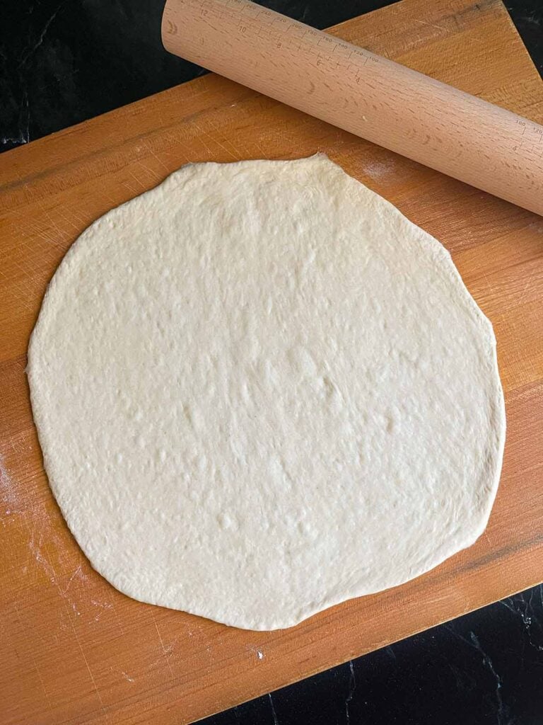 Pizza dough rolled out on a large wooden cutting board.