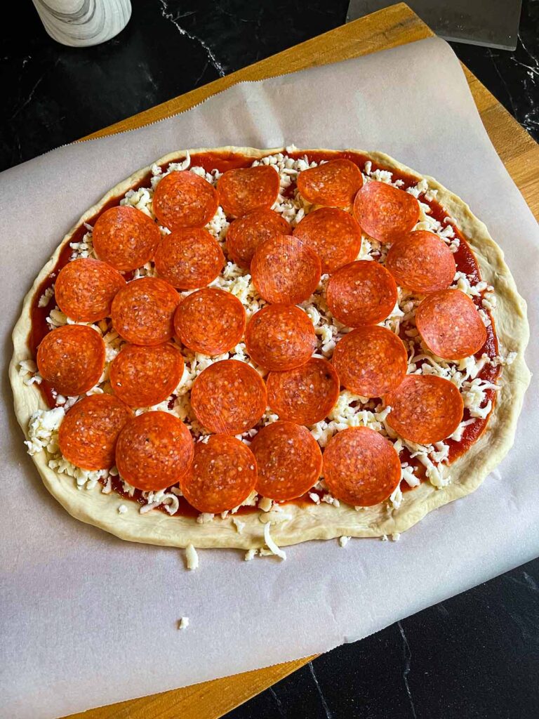 An unbaked pepperoni pizza on parchment paper.