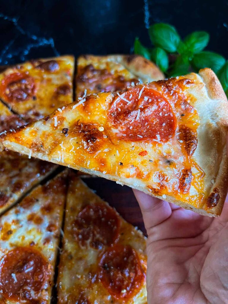 Holding up a homemade pepperoni pizza slice using homemade pizza dough.