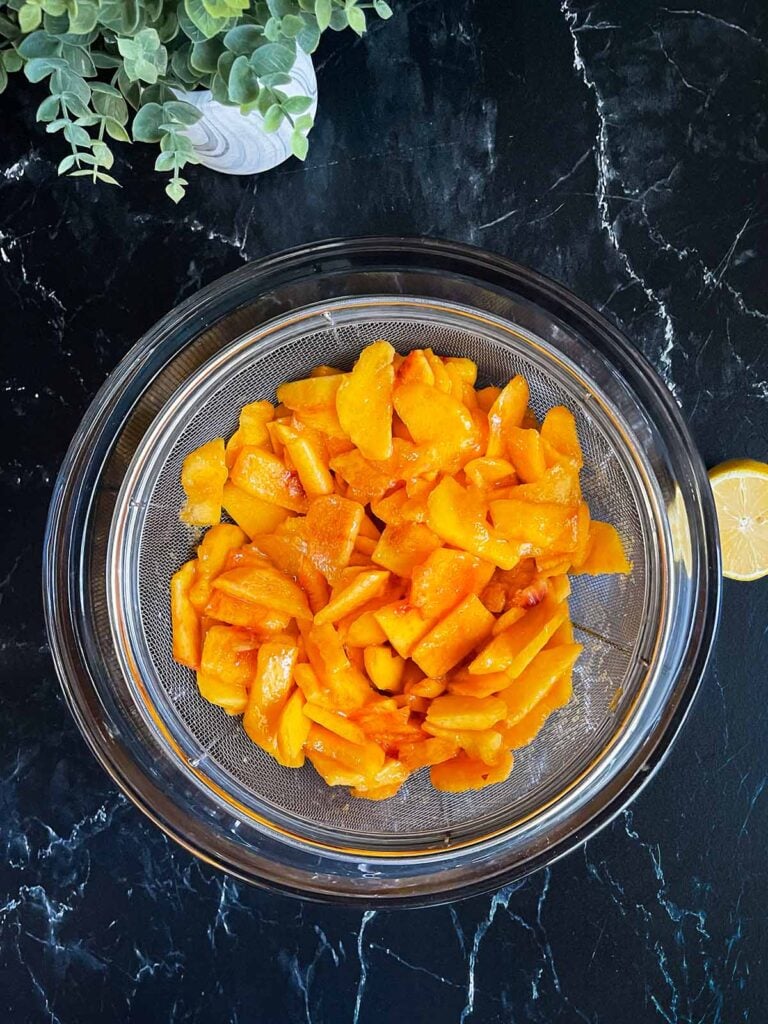 Peaches being drained in a glass bowl.