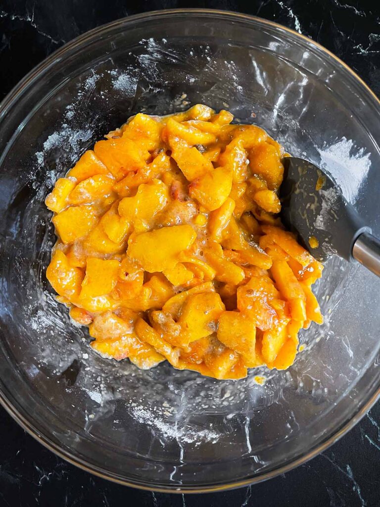 Peaches coated in the spice mixture in a glass bowl.