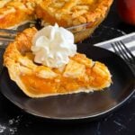 A slice of peach pie with whipped cream on a dark plate.