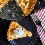 A slice of peach pie with whipped cream on a dark plate.