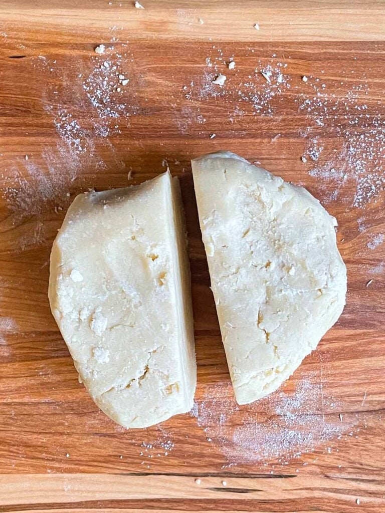 Pie crust dough divided on a cutting board.