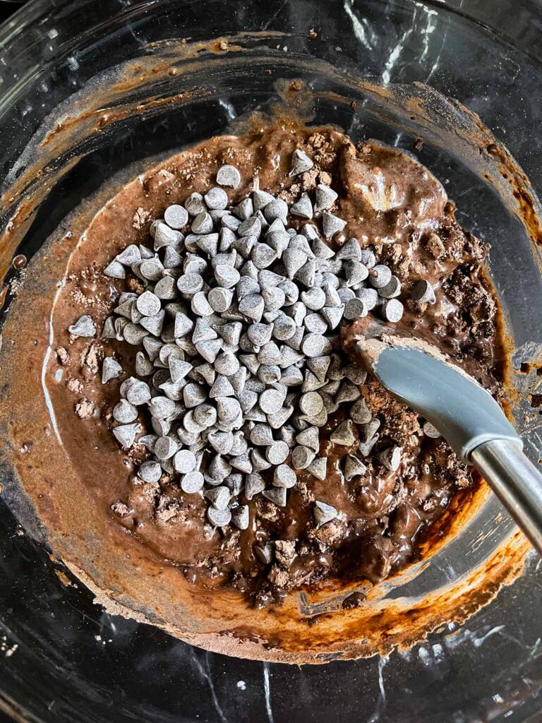 Adding the chocolate chips top the ingredients for double chocolate muffins in a large glass bowl.