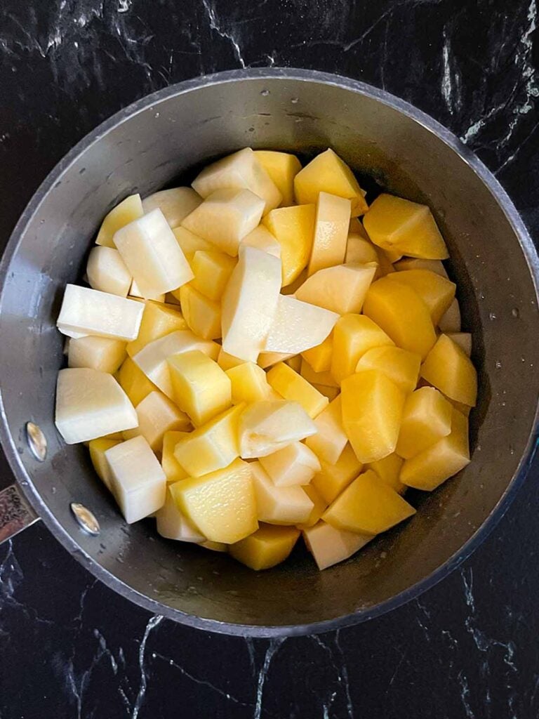 Raw cubed potatoes rinsed in a saucepan.