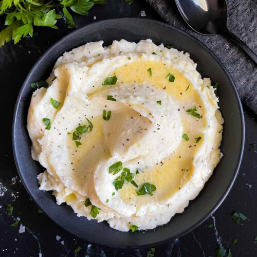 Garlic herb mashed potatoes in a dark bowl on a dark surface.