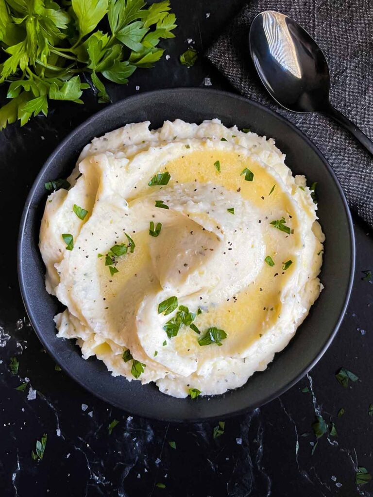 Garlic herb mashed potatoes in a dark bowl on a dark surface.