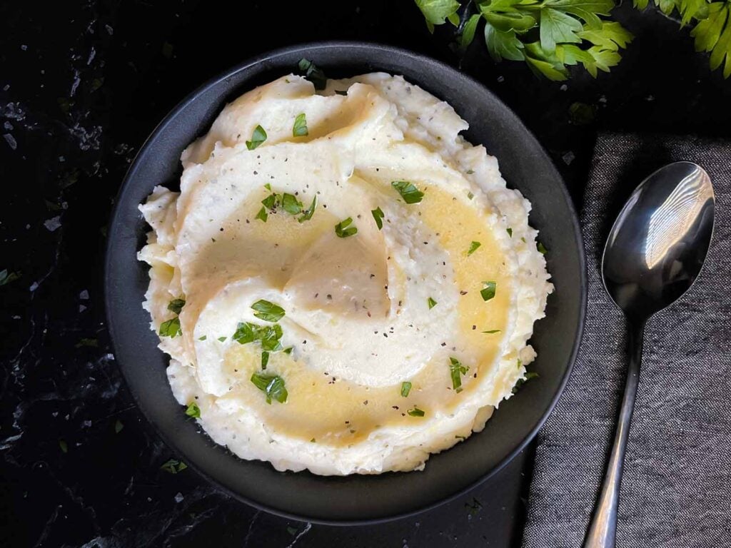 Garlic herb mashed potatoes garnished with melted butter and chopped flat leaf parsley.