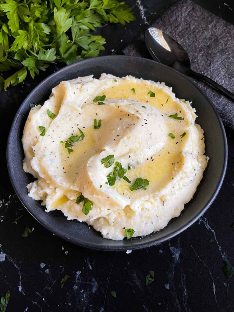 Garlic herb mashed potatoes garnished with melted butter and chopped flat leaf parsley.