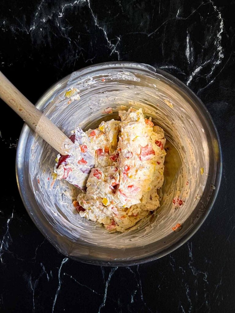 Ingredients for a cream cheese mixture for italian pinwheels mixed together in a silver mixing bowl on a dark surface.