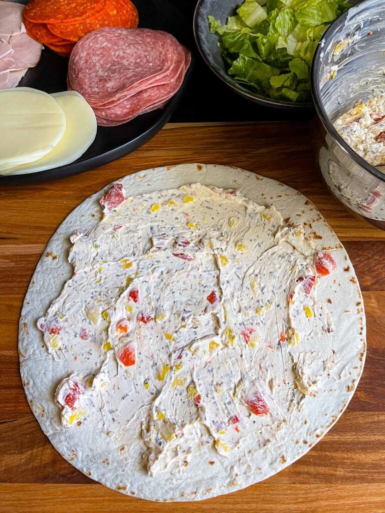 Cream cheese mixture spread across the surface of a large flour tortilla.