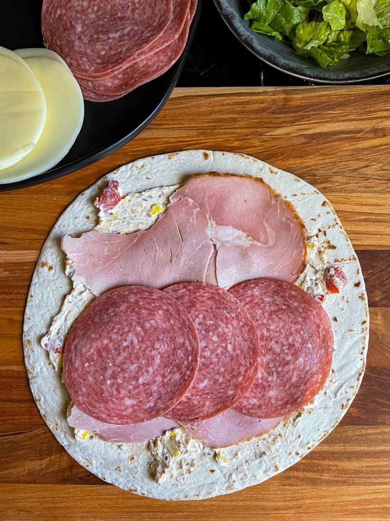 A layer of salami on the italian pinwheel as it's being made.