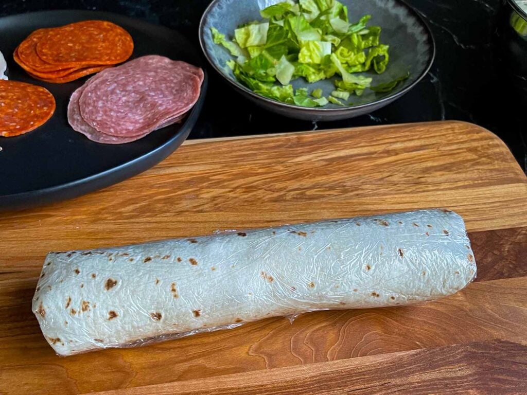 An Italian pinwheel, wrapped up in plastic wrap, unsliced.