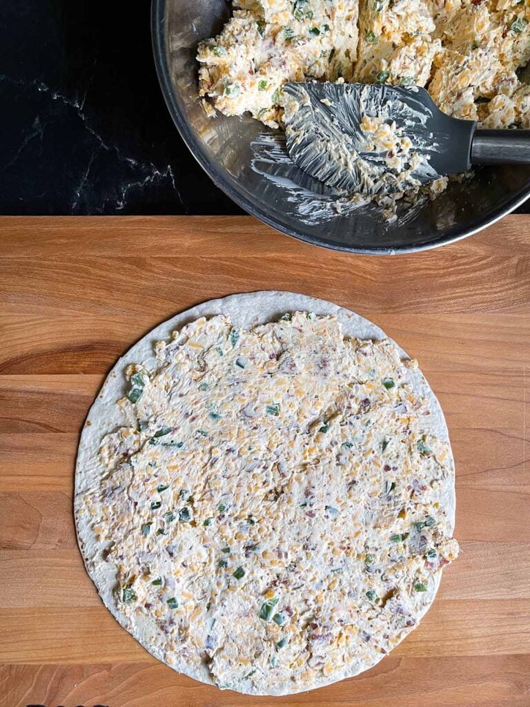 Spreading the jalapeno popper mixture across a tortilla.