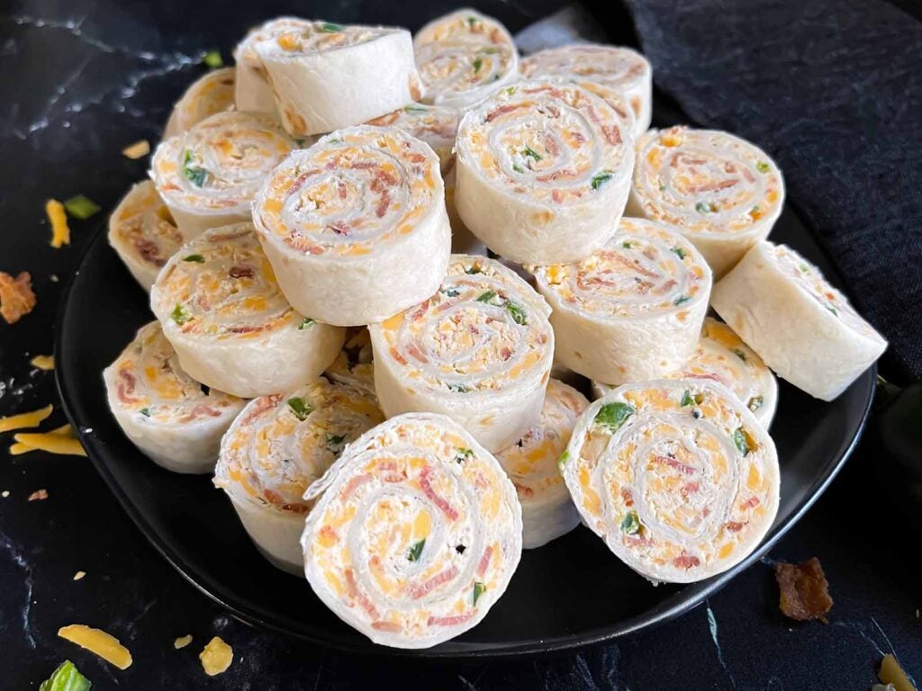 Jalapeno popper pinwheels on a dark plate on a dark surface.