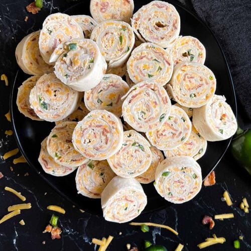 Jalapeno popper pinwheels on a dark plate on a dark surface.