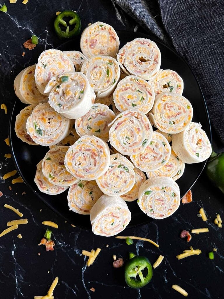 Jalapeno popper pinwheels on a dark plate on a dark surface.