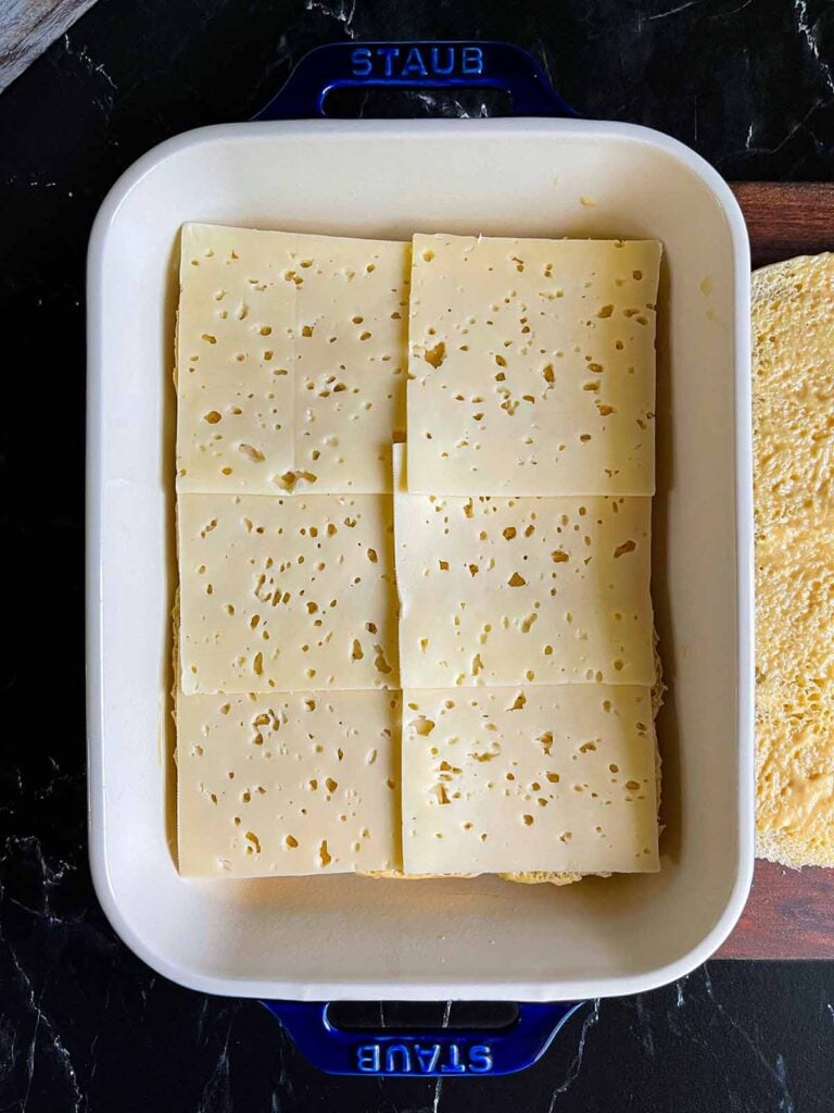 Swiss cheese layered over slider rolls in a baking dish.