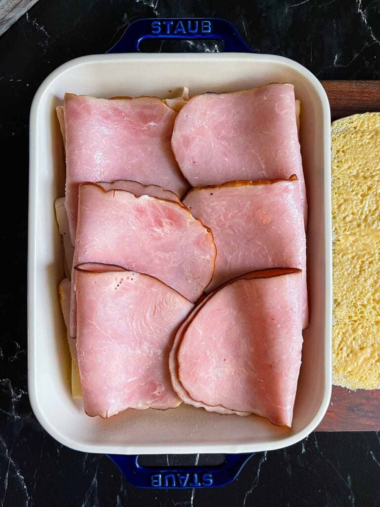 Ham layered over slider rolls in a baking dish.