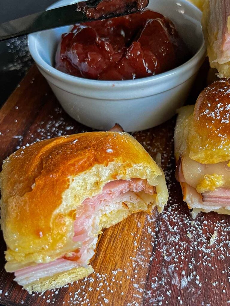 Monte Cristo sliders stacked up on a dark cutting board, one has a bite out of it.