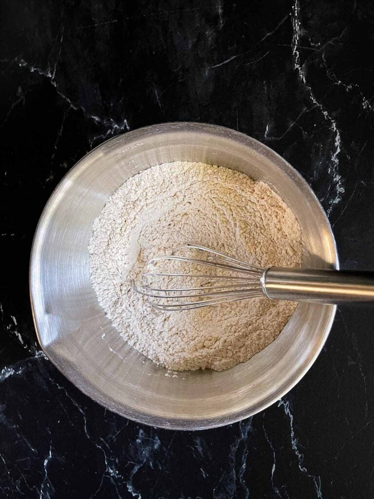 Dry ingredients for the old fashioned oatmeal raisin cookies mixed together in a silver bowl with a whisk.