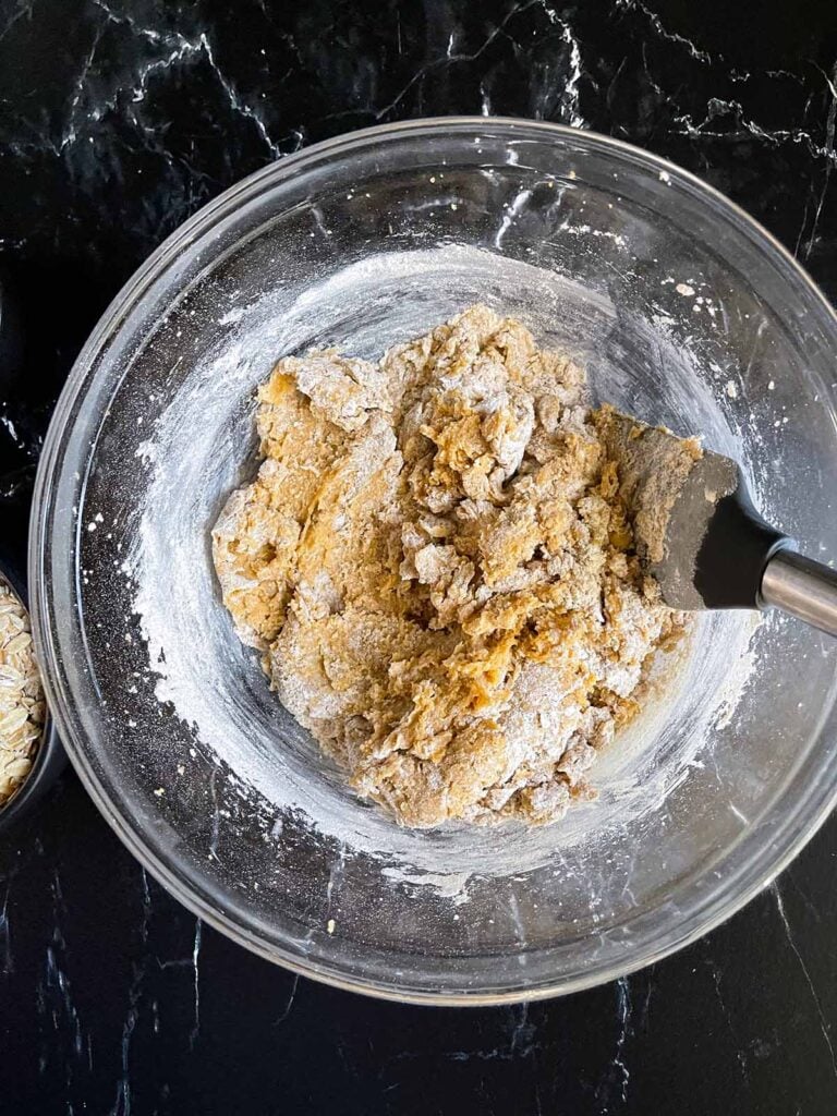 Flour folded in to creamed ingredients for oatmeal raisin cookies in a glass bowl.