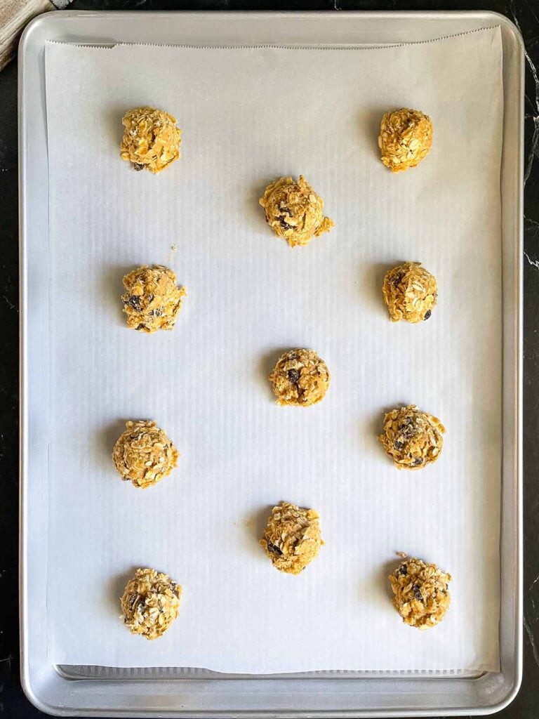 Old fashioned oatmeal raisin cookie dough balls on a parchment paper lined baking sheet.