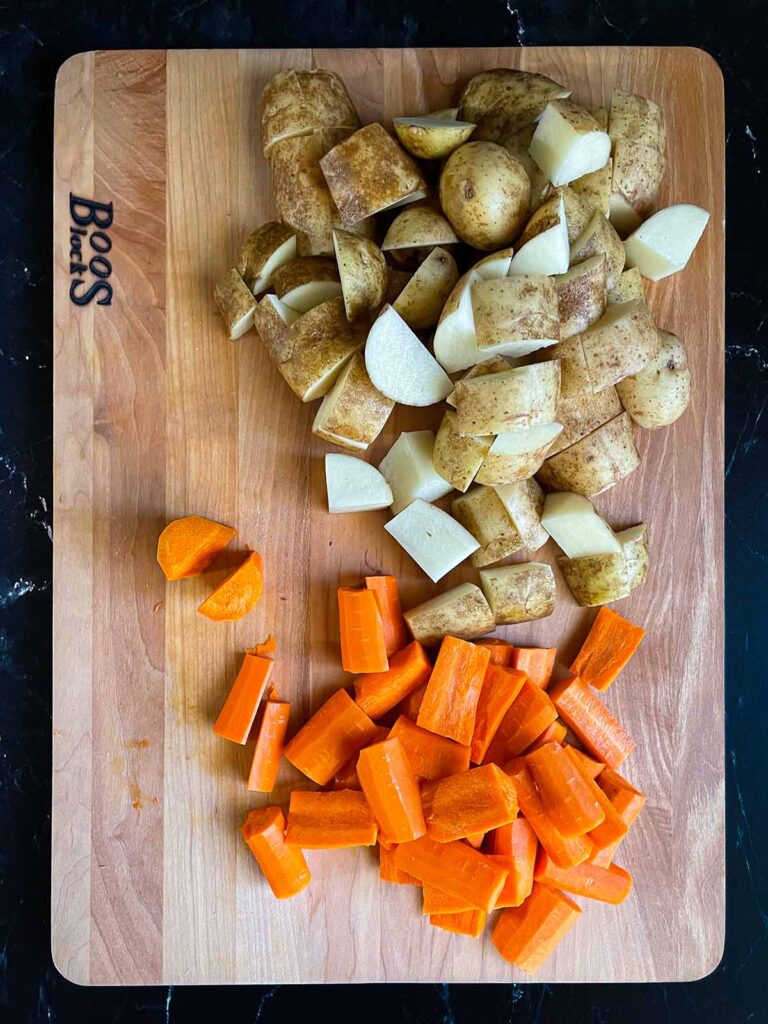 Cut raw potatoes and carrots on a wooden cutting board.