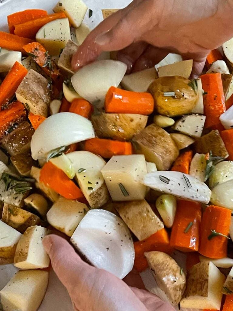 Chicken thighs, potatoes, carrots, onions, and garlic tossed in seasonings and olive oil in a lined baking sheet.