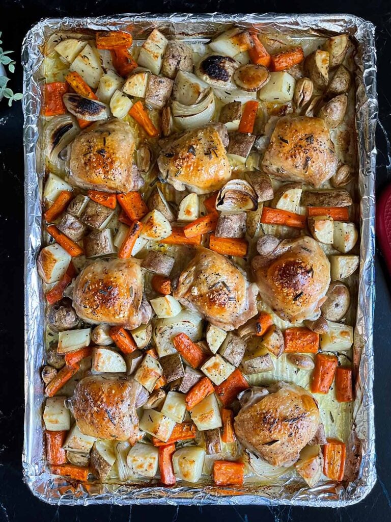 One pan roasted chicken and vegetables in a foil and parchment paper lined baking sheet.