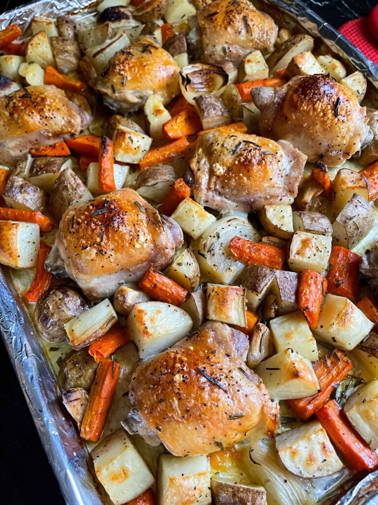 One pan roasted chicken and vegetables in a foil and parchment paper lined baking sheet.