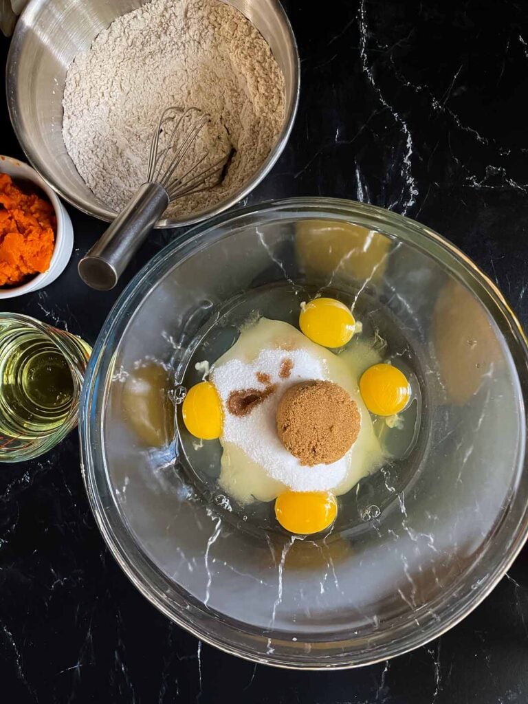 Eggs, sugars, and vanilla extract for pumpkin bread in a glass bowl.