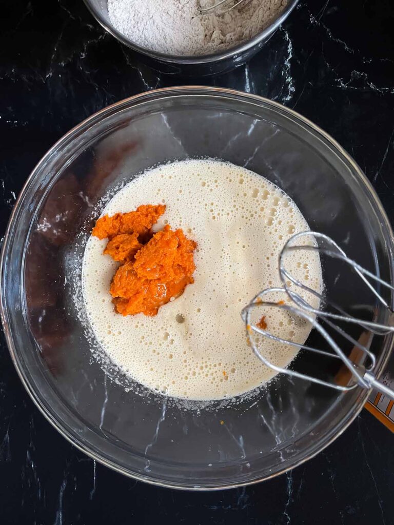 Pumpkin puree and vegetable oil added to the wet ingredients in a glass bowl.