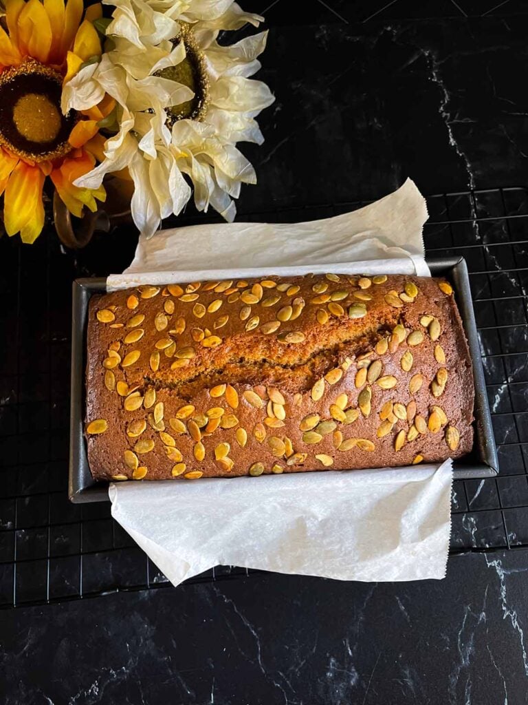 Baked pumpkin bread in a loaf pan on a dark surface.