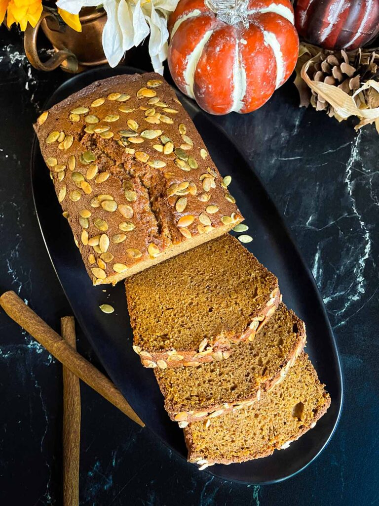 Baked pumpkin bread, sliced, on a dark platter.